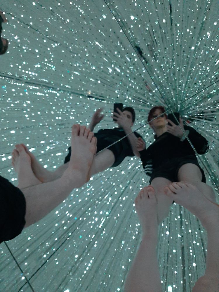 selfie on a mirrored floor of LED light strips hanging from ceiling