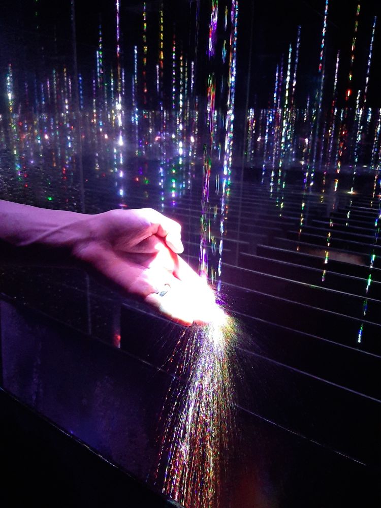 a hand interrupting a stream of neon-lit water