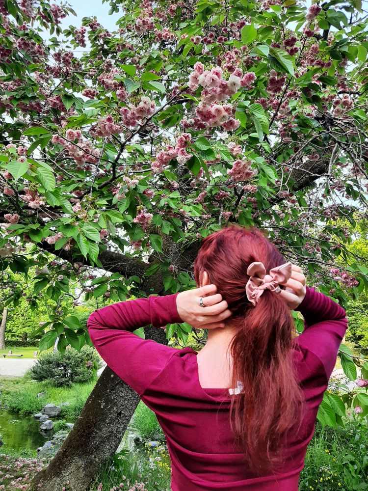 Claire in red shirt and pink hair tie in front of blooming cherry blossom tree in Kyoto