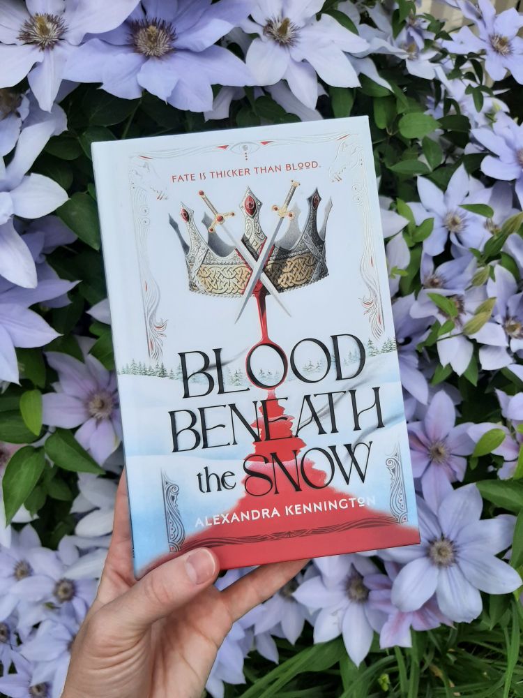 Photo of the book Bl00d Beneath the Snow in front of a flowering clematis 