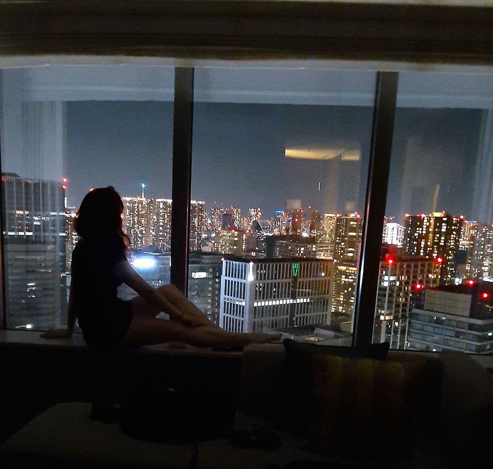 photo of Claire sitting in hotel windowsill, silhouetted by Tokyo at night