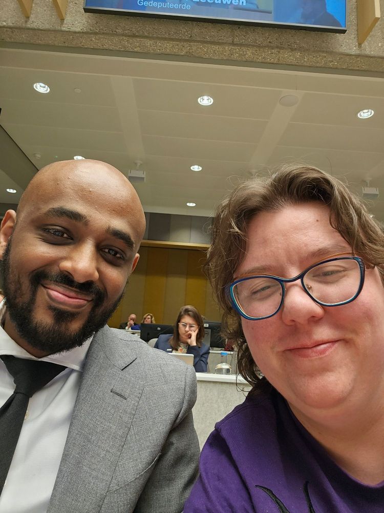 Selfie van Adem Mustafa Negash en ik in de statenzaal van Zuid-Holland, met in de achtergrond Camille hard aan het werk.