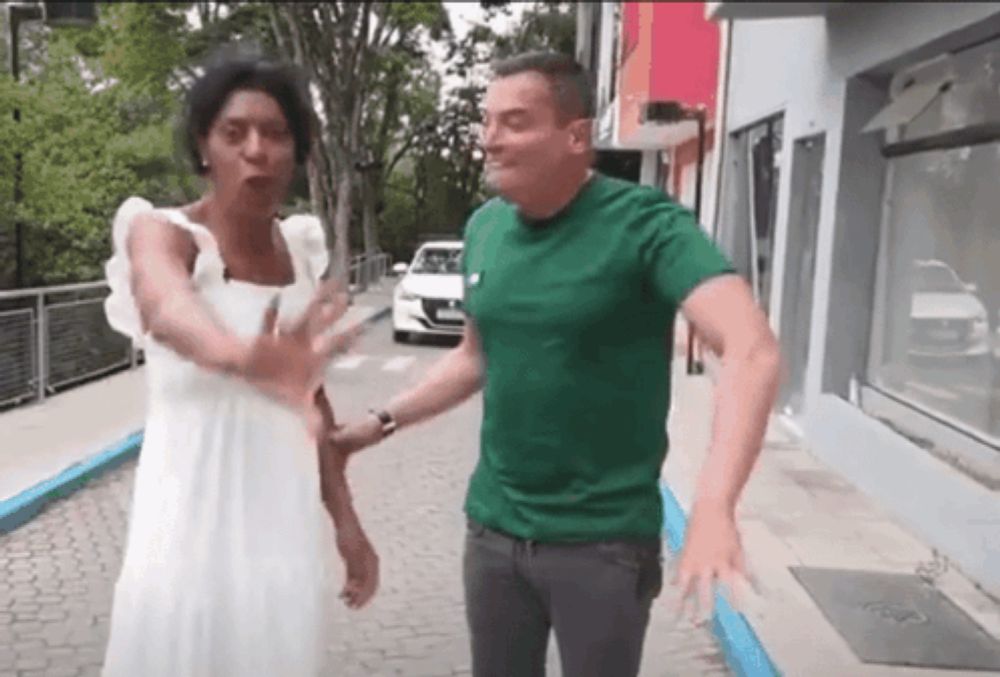 a man in a green shirt is standing next to a woman in a white dress on a sidewalk