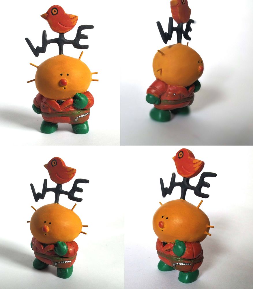 Vane, a yellow character with small dot eyes, a round orange nose, and a weather vane with an orange bird on his head. He's wearing an orange boiler suit with green gloves and boots, and a brown waist bag.