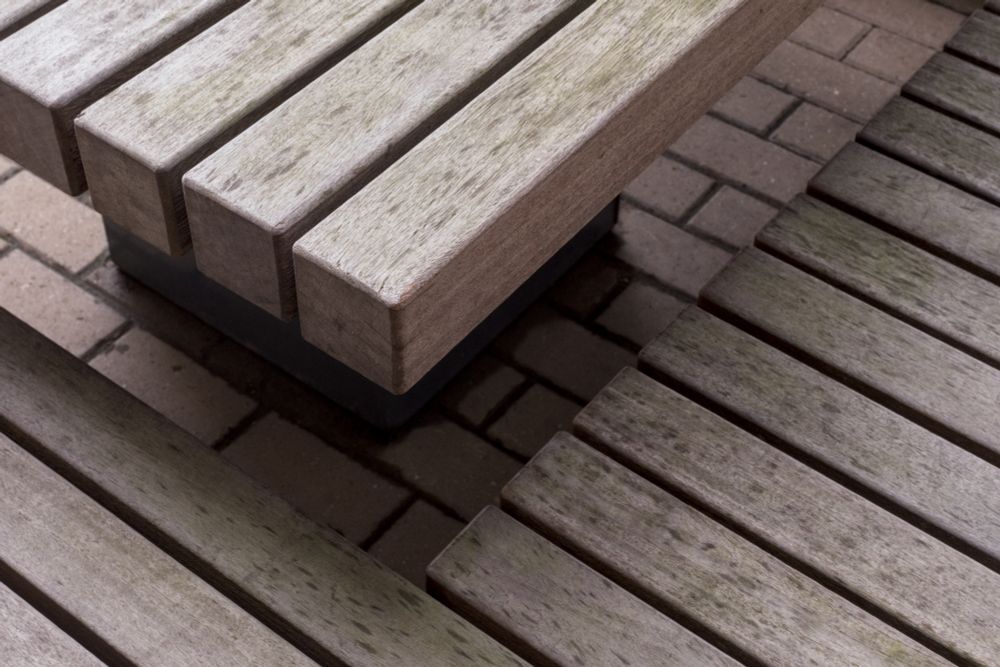 Parts of a wooden bench and table viewed from above and at a diagonal.  Between the bench and the table a brick patio can be seen.  