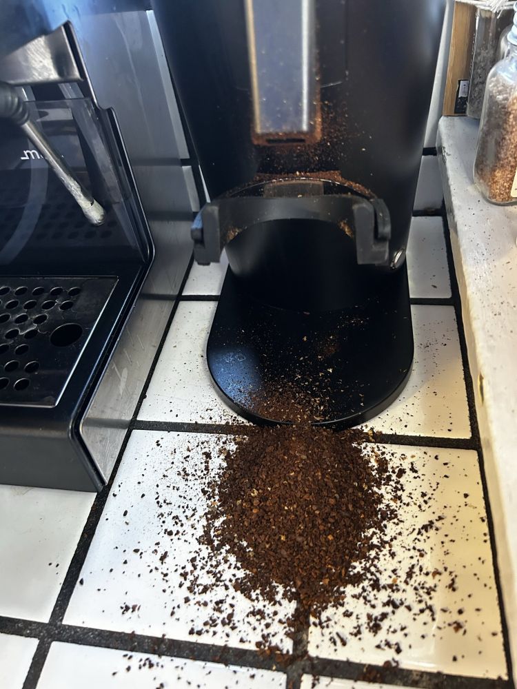 A coffee grinder that was recently used incorrectly such that the grounds fell onto the counter in front of it rather than into a receptacle. 