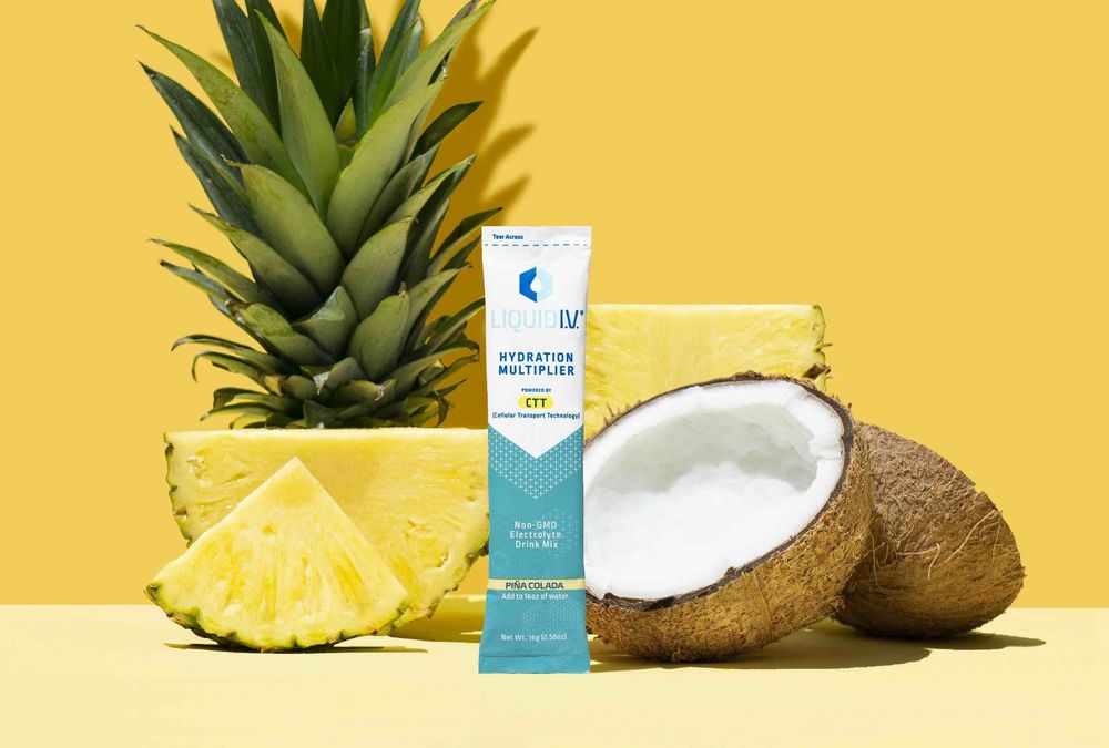 Picture of a packet of Liquid IV in the pina colada flavour with pineapple and coconut in the background