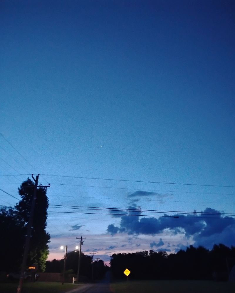 Blue clouds above a road trees and power lines.