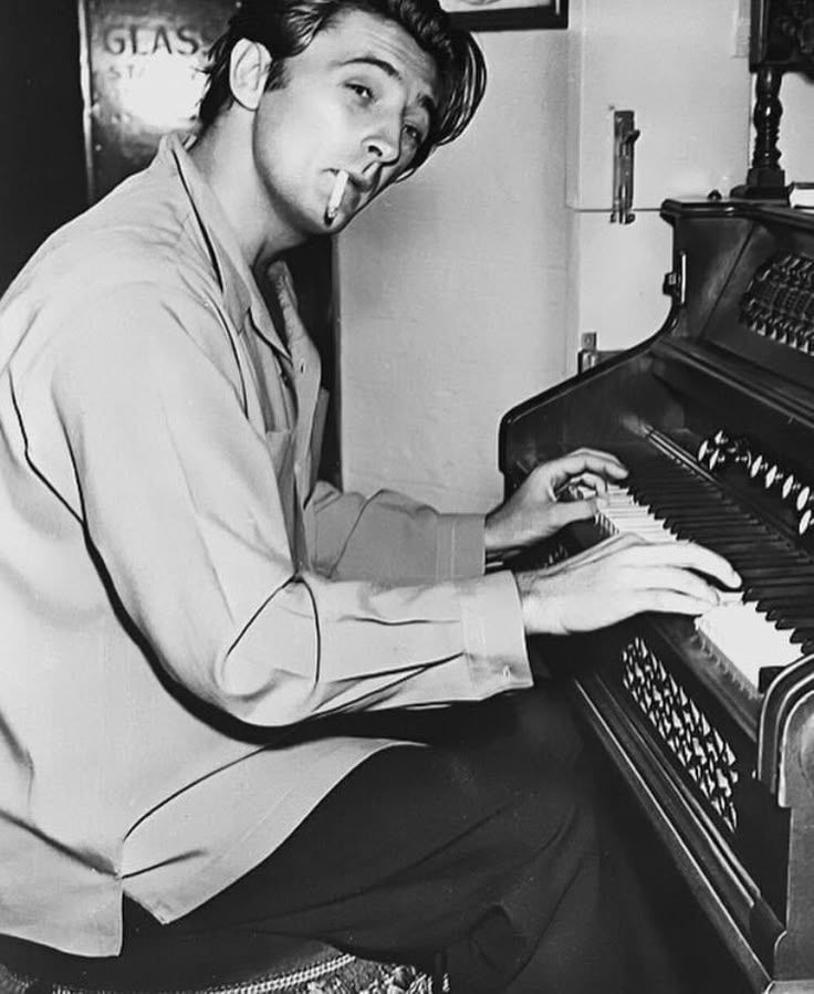 Robert Mitchum playing piano and smoking a cigarette.