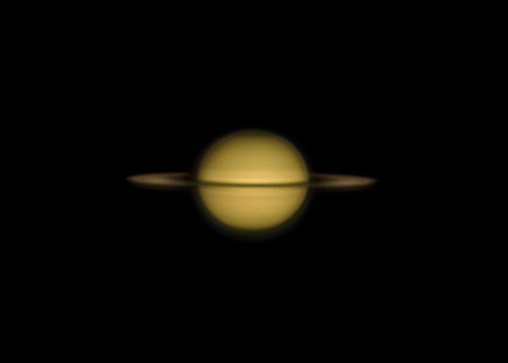 picture of a pale golden saturn showing the rings at a shallow angle and horizontal lines on saturn showing cloud bands. one of the lines is the rings. the shadow of saturn on the rings can be seen on the left