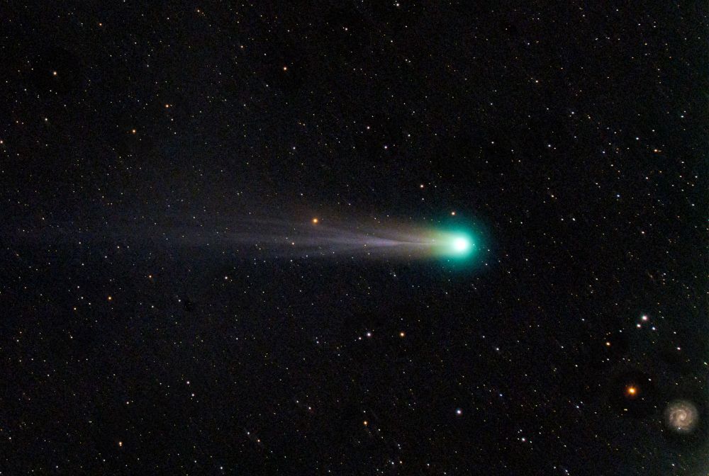 image of a comet with a spiral galaxy in the lower right corner