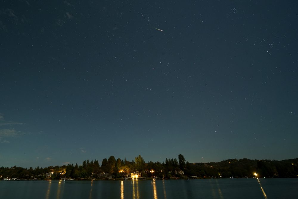 a meteor steaks across a starry sky over a lake