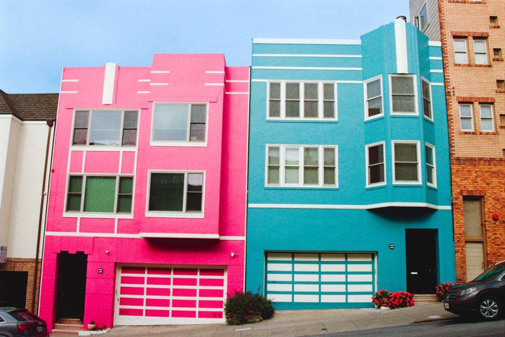 Two art deco rowhomes next to each other, one pink and the other soft blue, on a slight incline