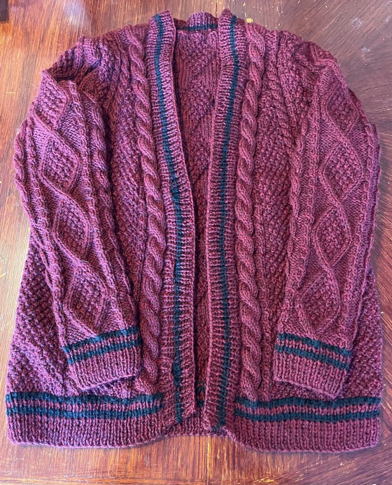 A mostly finished folklore cabled cardigan in garnet main color with black accent stripes. Front view.