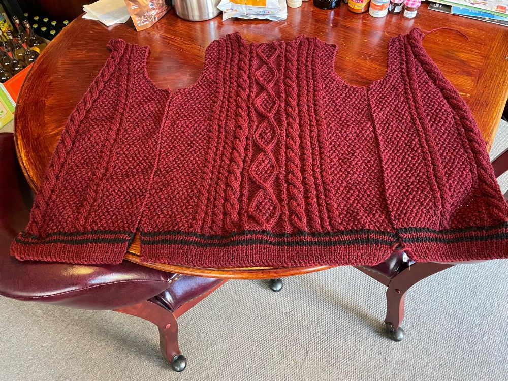Back and side pieces of a folklore (cabled) cardigan yet to be seamed. Main color is garnet with black accent stripes.