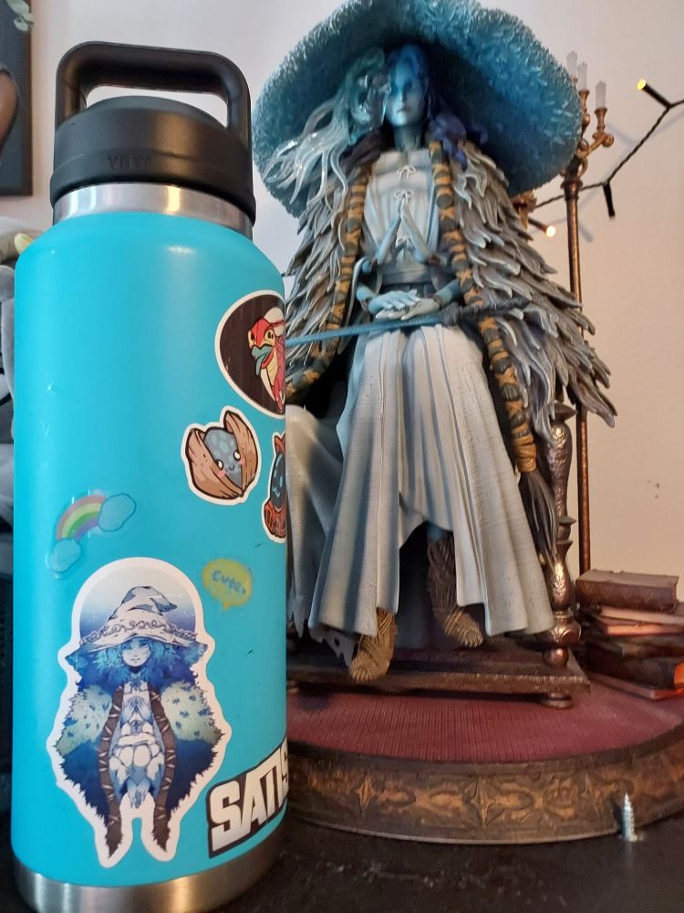 Water bottle with a sticker of Ranni the Witch next to a big statue of Ranni
