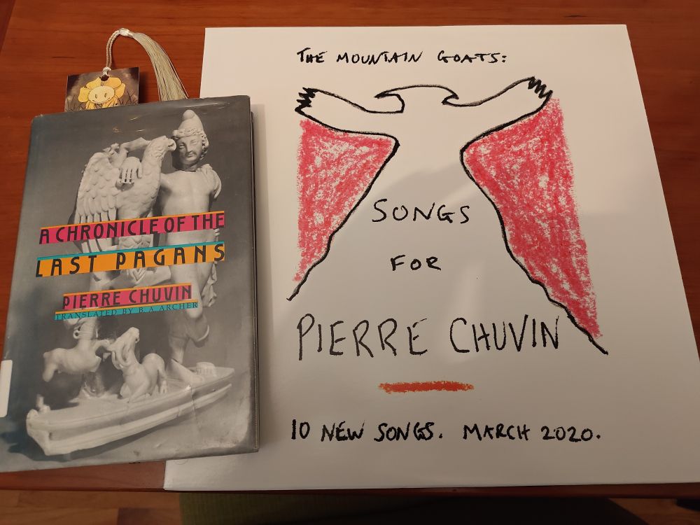 Pierre Chuvin's A Chronicle Of The Last Pagans (Chicago Public Library copy) next to the Mountain Goats' Songs For Pierre Chuvin (on vinyl).

There's a bookmark in the book, the kind with the little tail tied into the top, peaking out just enough that you can see a friendly yellow flower, with eyes and an inscrutable expression, peaking out of the top. I think it was a Kickstarter bonus for an art book by Undertale fans.