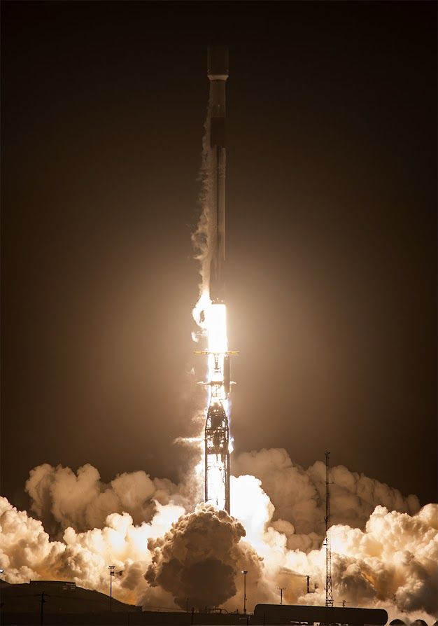 Rocket taking off at night, leaving trail of flames behind with low billowing clouds against the ground.