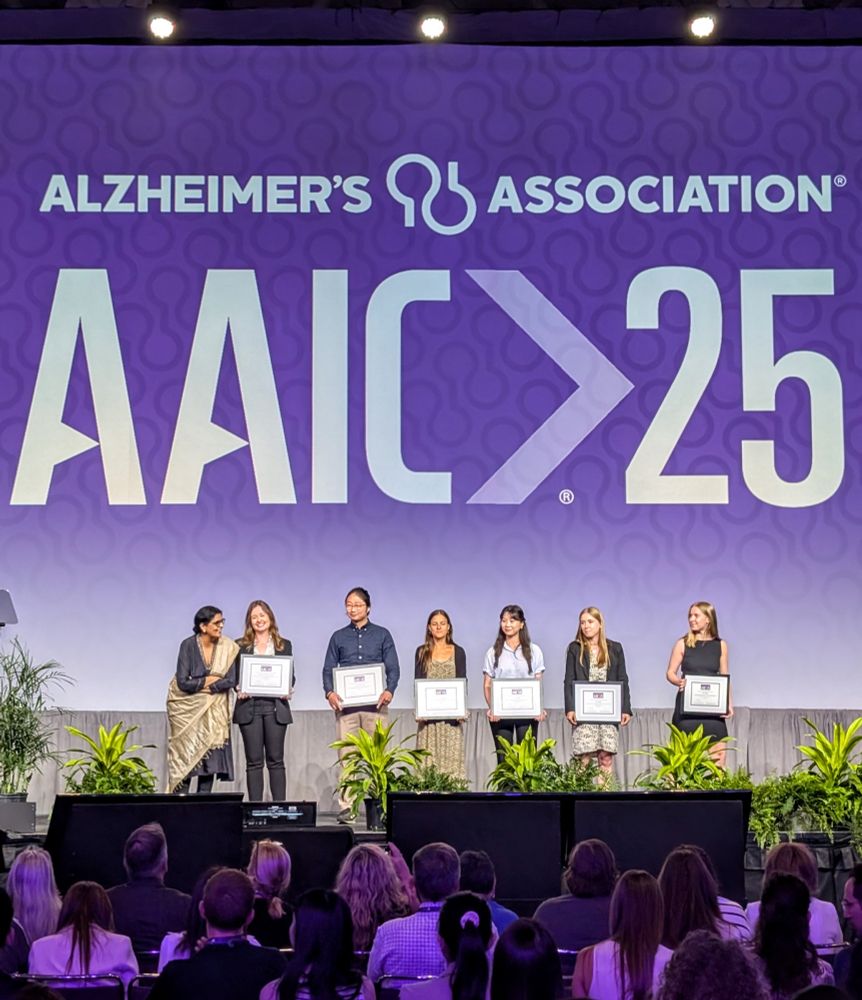 Winners of the #AAIC25 Poster Competition stand on the stage and receive their awards.