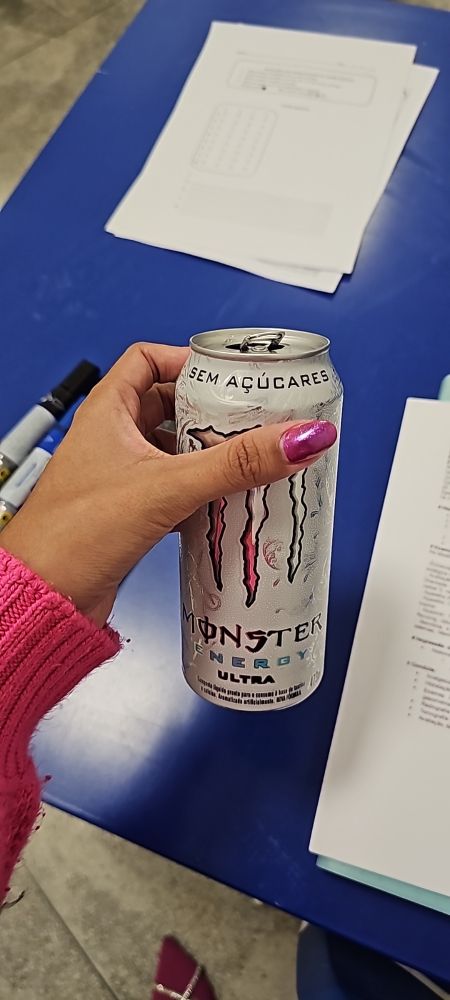 Lata de energético de 473 ml. Ao fundo provas e gabaritos e pincéis de quadro branco