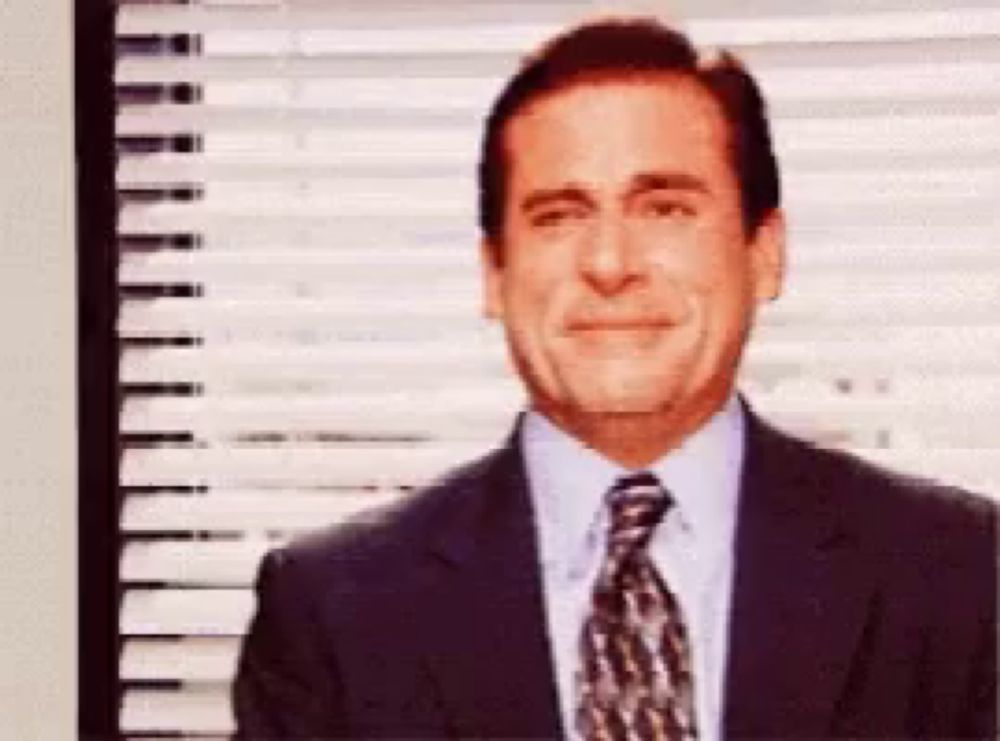 a man in a suit and tie smiles in front of a window