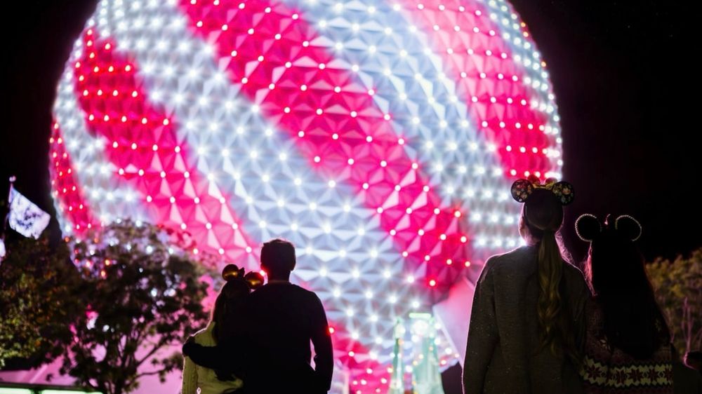 People look up at Spaceship Earth in EPCOT lit up with red and white candy cane stripes. 