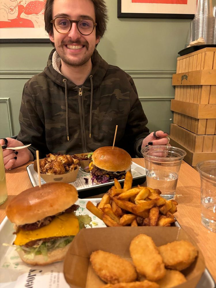 Moi grand sourire, face à deux burgers vegans, des frites, des nuggets vegans, du soja en sauce barbecue et des choux-fleurs braisés