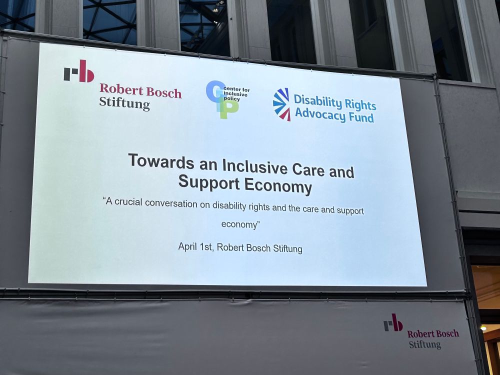 Projection on the wall that shows 3 organisational logos and reads Towards an Inclusive Care and Support Economy