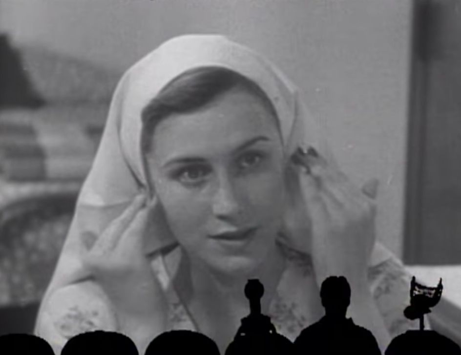 Young woman in the short sitting at a vanity doing facial routine with a head cloth, also there's the shadow of Joel and the bots from MST3K 