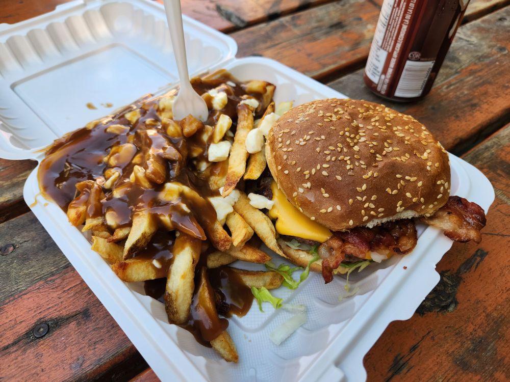 A styrofoam clamshell with a bacon cheeseburger in the corner with the rest filled with fries, cheese curds, and gravy in an alchemical mixture that is greater than the sum of those three parts.