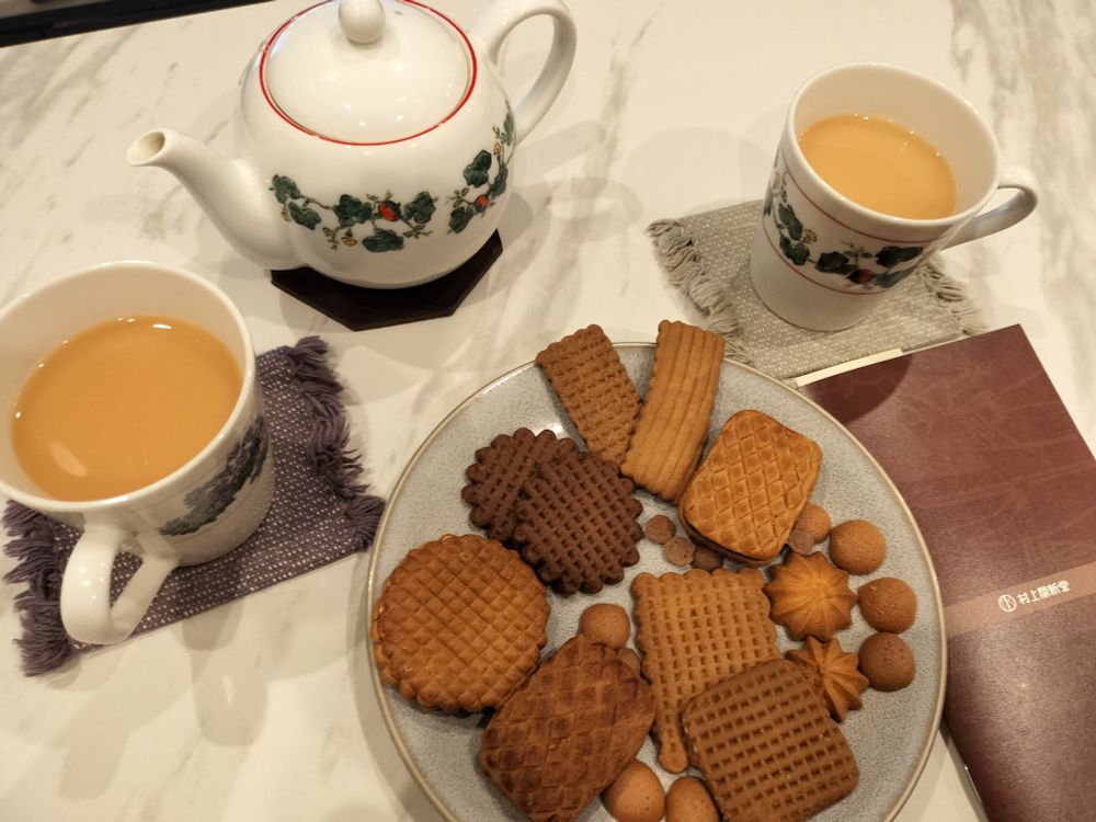 白いテーブルの上に六花亭ロゴのティーポットとミルクティーの入ったマグカップ。あと村上開進堂のクッキーがお皿に載っている