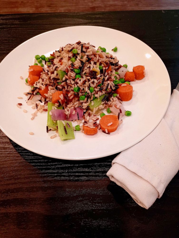 A plate of wild rice with carrots, celery, onions, and peas. The food is very tasty, but the cook neglected to properly chop the veggies, and they are in big chunks instead of aesthetically pleasing slices. 