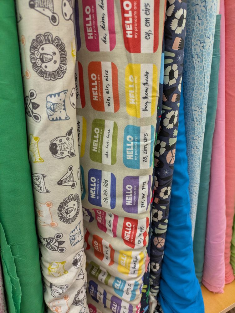A fabric printed with multicolored "hello my pronouns are" and different pronoun options.