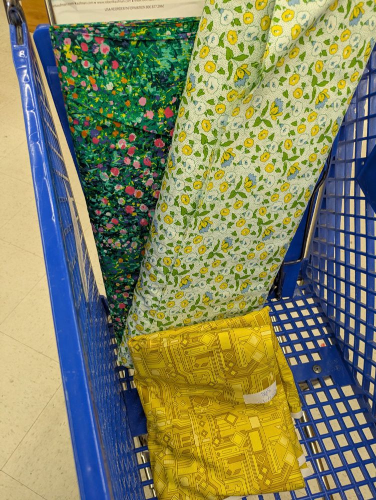 A green impressionist floral fabric, a green and yellow sort of 70s floral fabric, and a dark yellow fabric with a sort of linear, electronic, or architectural print. 