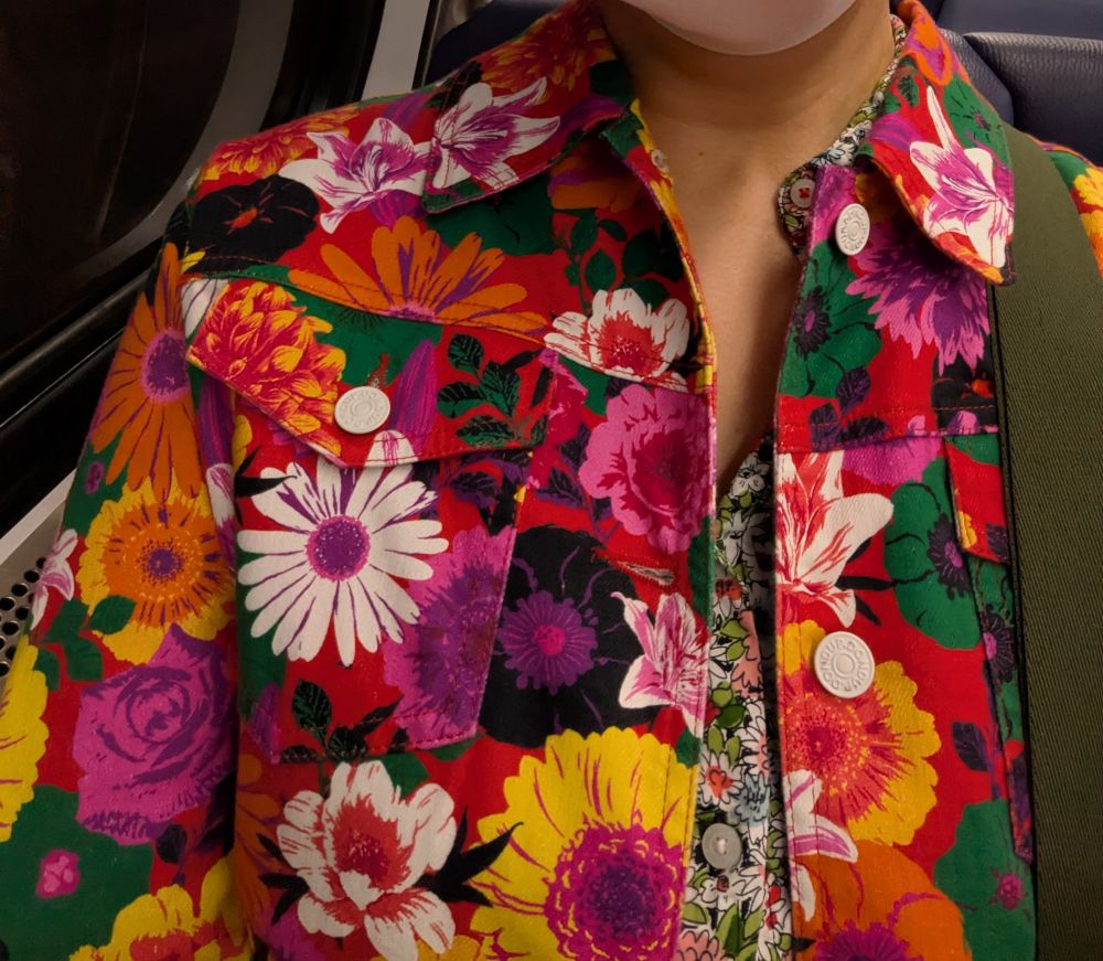 I am wearing a denim jacket that is red with a large white, hot pink, yellow, green, purple, and black floral print. 