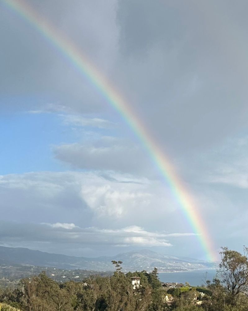 A rainbow arches across a semi-cloudy sky toward the ocean