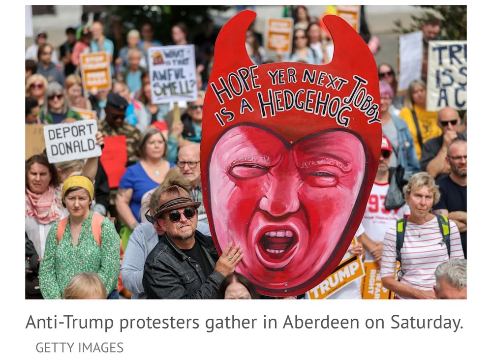 Image from Getty showing protesters in Scotland holding up placards one of which shows a pink faced Trump adorned with what appear to be Satan horns and a slogan across his forehead "Hope yer next jobby is a hedgehog".