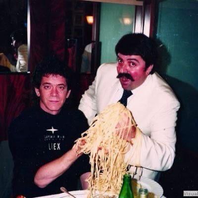 Lou Reed and a mustachioed gentleman holding up handfuls of spaghetti