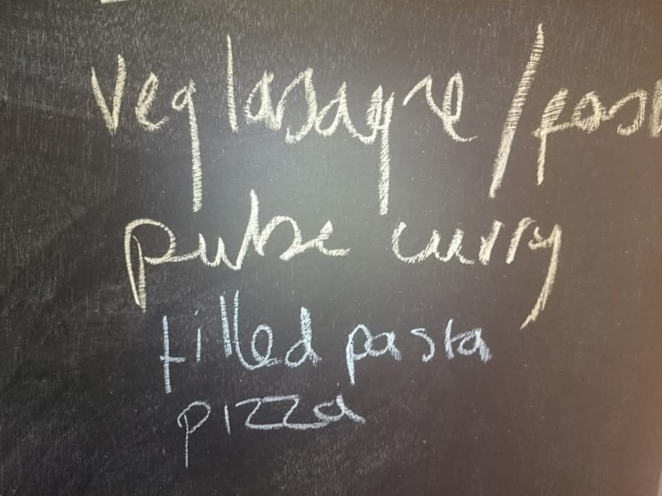 A chalk board showing veg lasagne. Filled pasta. Pizza. And what for all the world looks like "pube curry"