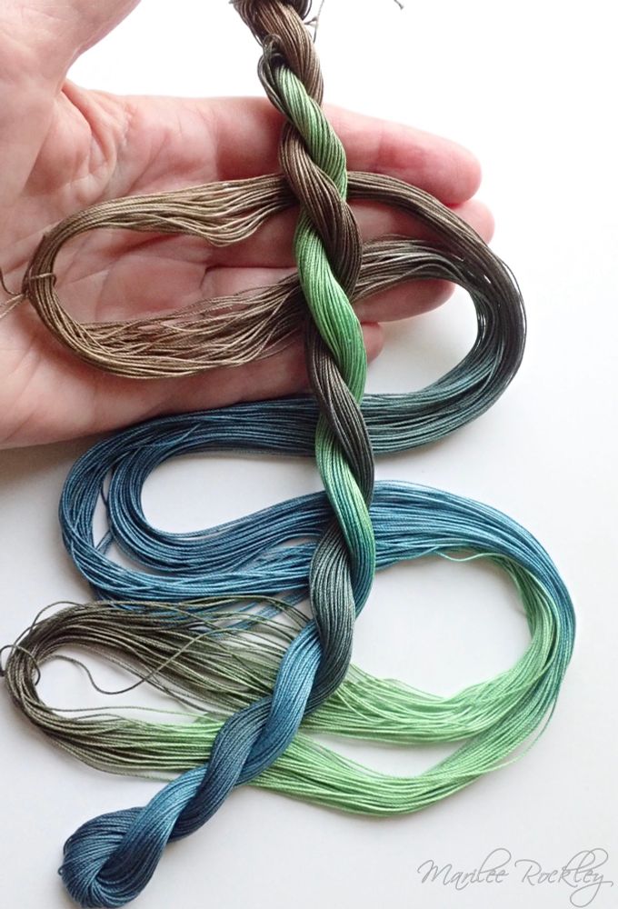 2 skeins of hand dyed thread packed, one twisted and one open to show the color gradation. The colors shade from brown, green, and teal. The thread is displayed on a hand, giving a reference to the thread size, which is suitable for lacemaking purposes.