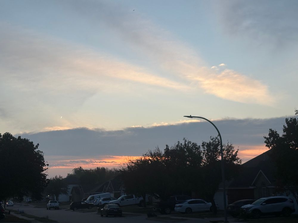 Sunrise behind clouds on a tree lined neighborhood street. 