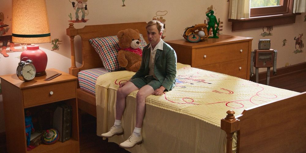 Nathan Fielder pretending to be a child sitting on a cartoonishly large bed