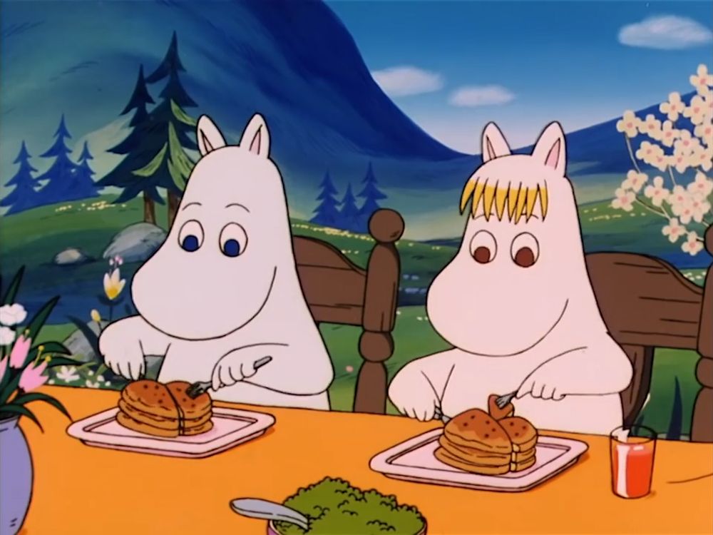 Moomin and Snorkmaiden eating pancakes at the table which is set outside.