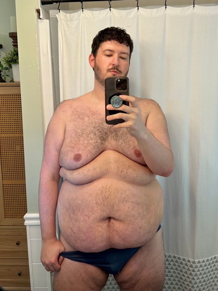 A man holding a phone, slightly tugging his briefs down