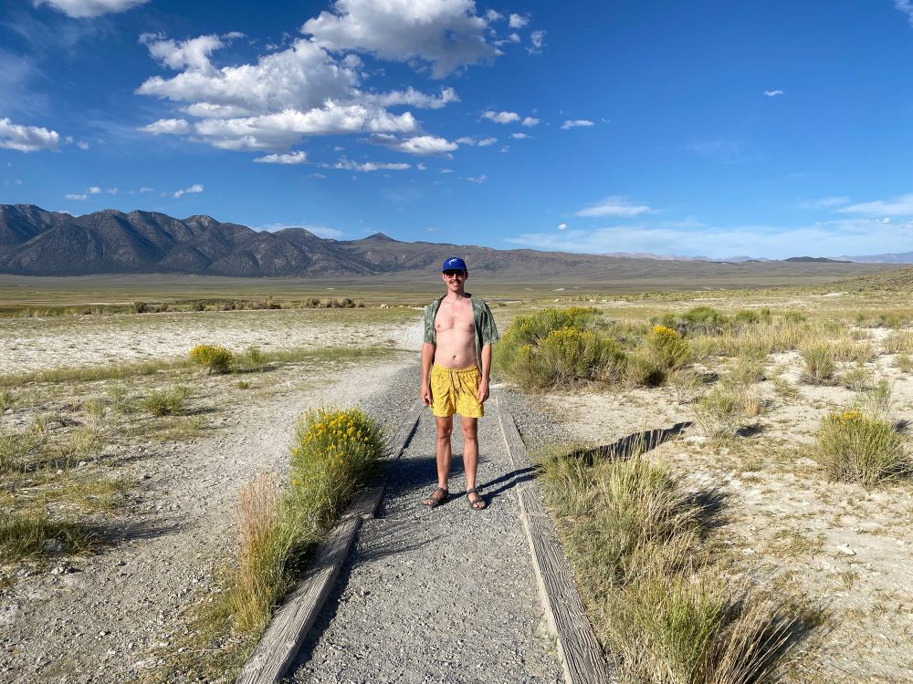 The author standing on a trail in a wide grassy valley with mountains in the background. 