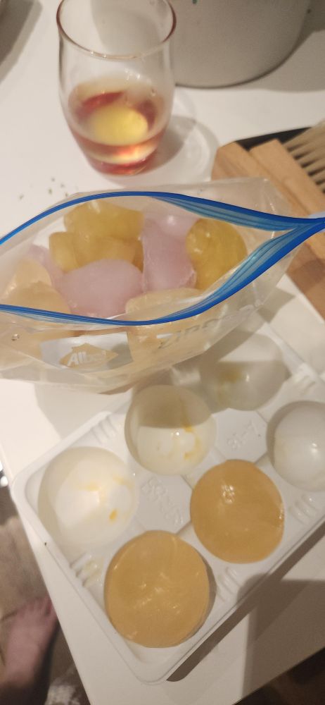Photo d'un sachet de congélation rempli de demi-sphères roses, orange et jaunes et d'un moule de six demi-sphères partiellement rempli de glaçons orange. 