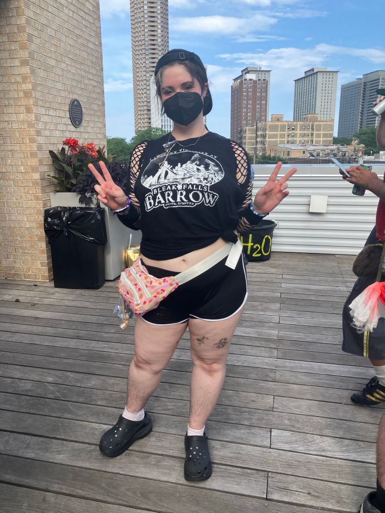 Full body picture of me on the rooftop at boots party in an all black outfit consisting of a hat, tank top, fishnet shirt, black shorts and crocs and a face mask 