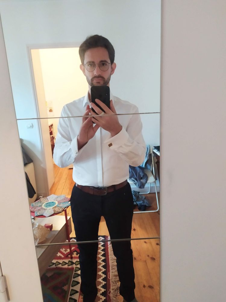 a guy (??? debatable ???) in a white button-up with cufflinks and black dress pants. Short beard, short hair, no life discernible in his eyes