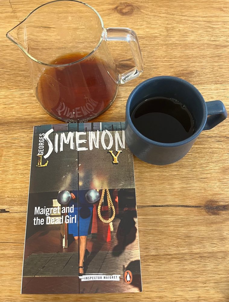 ‘Maigret & The Dead Girl’ photo cover shows a detail of a woman in a blue dress walking toward a set of glass doors. (Also a pour over coffee in cup & carafe.) 