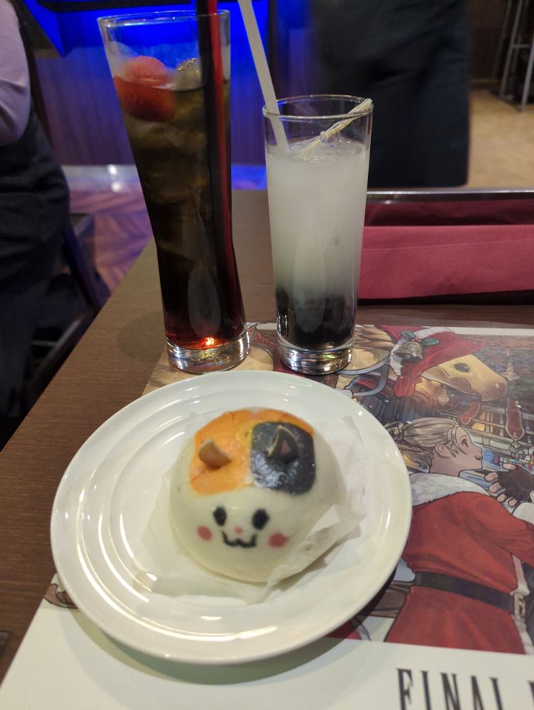 A dumpling stylised to look like a cute cat, accompanied by two cocktails (because decisions are hard).